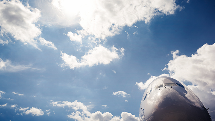 Die Spitze eines Flugzeugs mit Lufthansa Logo von unten vor einem blauen Himmel mit einigen Wolken
