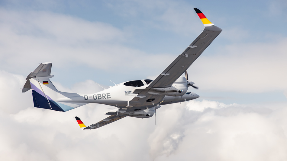 A small aircraft of type DA42 flies above the clouds in the blue sky.