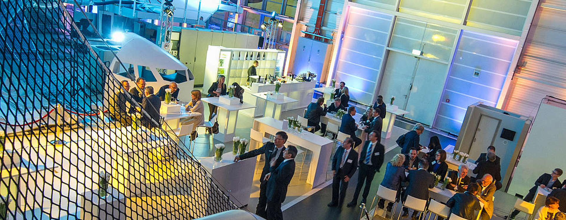 In a colourfully illuminated training centre there are bar tables and stools between the training equipment and around 30 guests