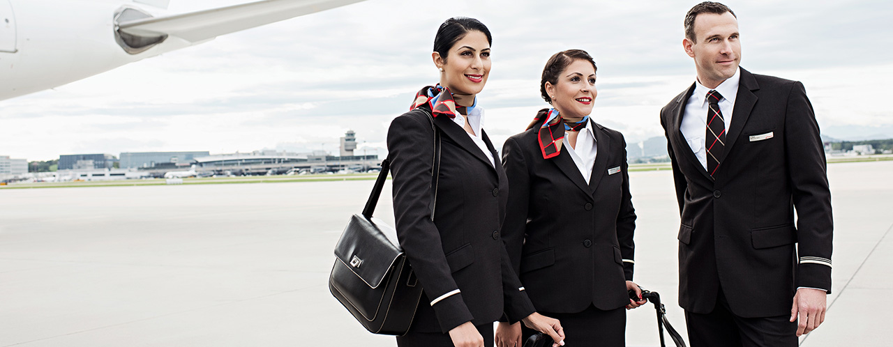 Two female and one male SWISS flight attendants stand with their luggage on a runway.