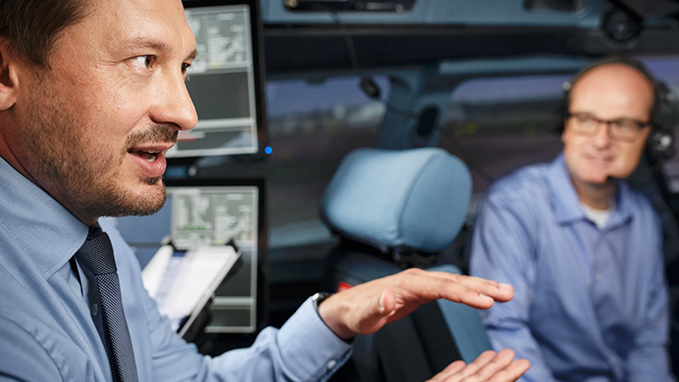 Blick auf das Cockpit eines Full Flight Simulators, in dem ein Pilot sitzt und ein Instructor etwas erklärt.