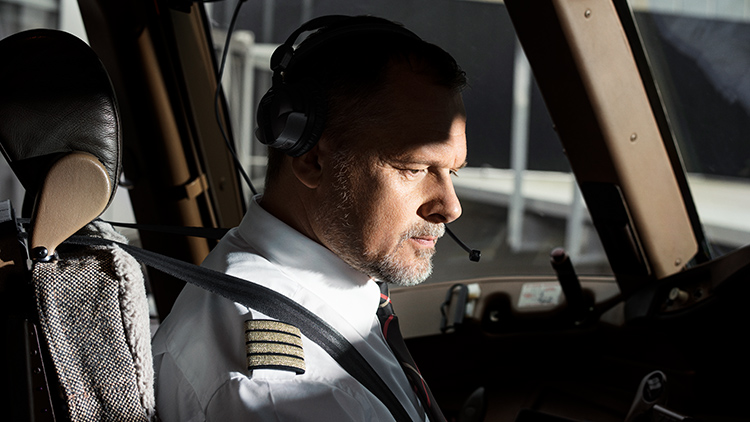 An elderly pilot with a full beard looks intently at Instruments in an aircraft cockpit