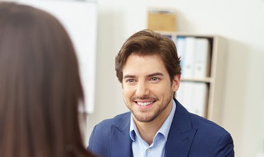 Eine Person unterhält sich lächelnd mit einer anderen Person, von der man nur den Hinterkopf sieht.