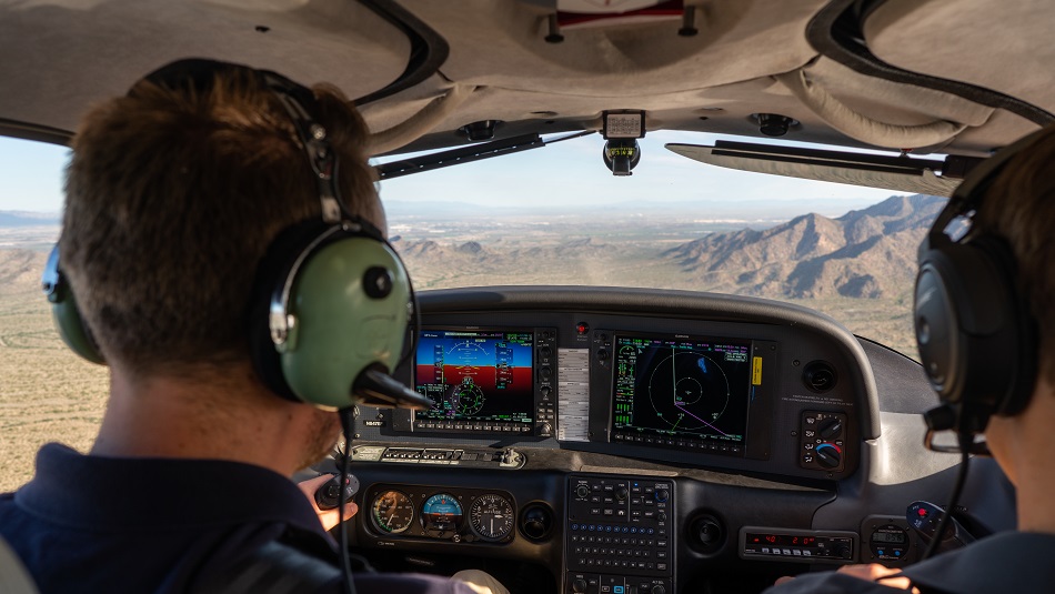 Two people sit in the cockpit of a training aircraft and steer the aircraft over the Arizona desert