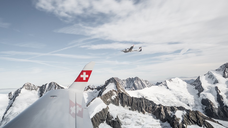 A training aircraft is flying over snow-covered mountains.